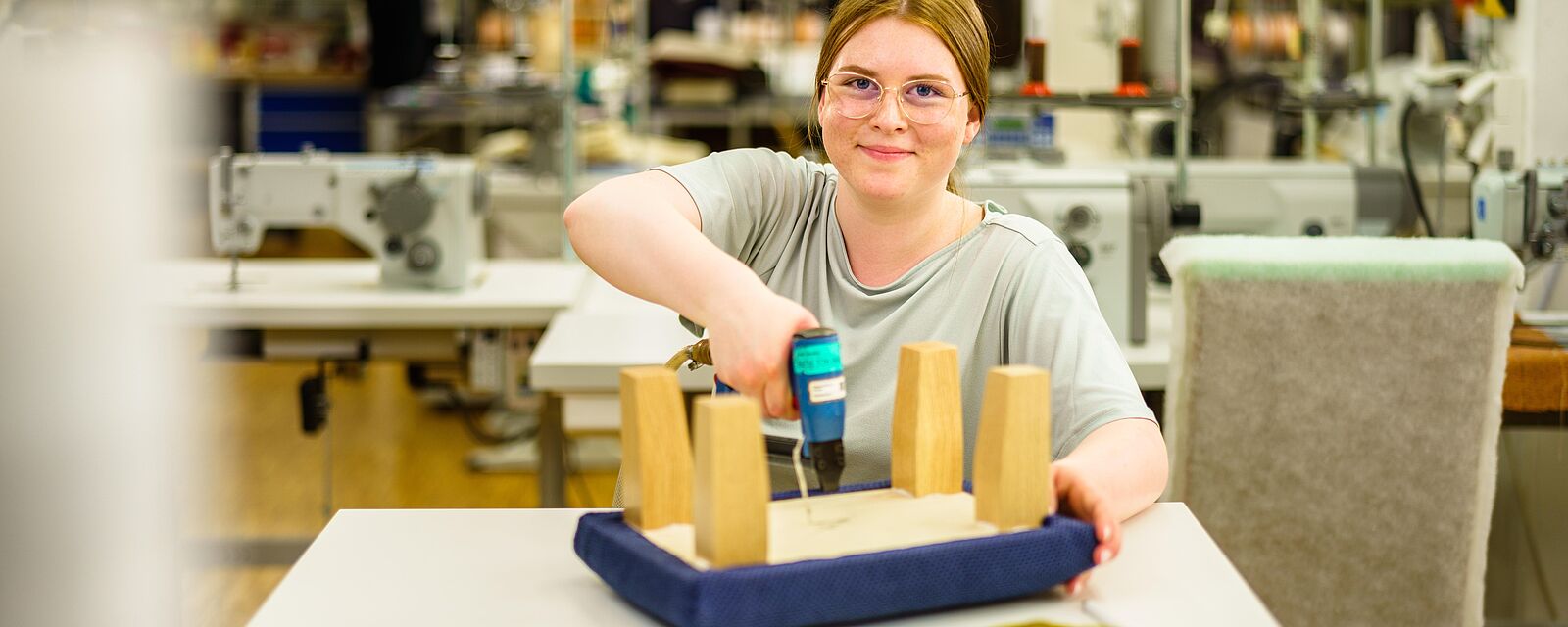 Für  die Herstellung des Junior-Meisterstücks befestigt Alisa N. blauen Stoff an einen Holzhocker mit einem Elektrotacker.