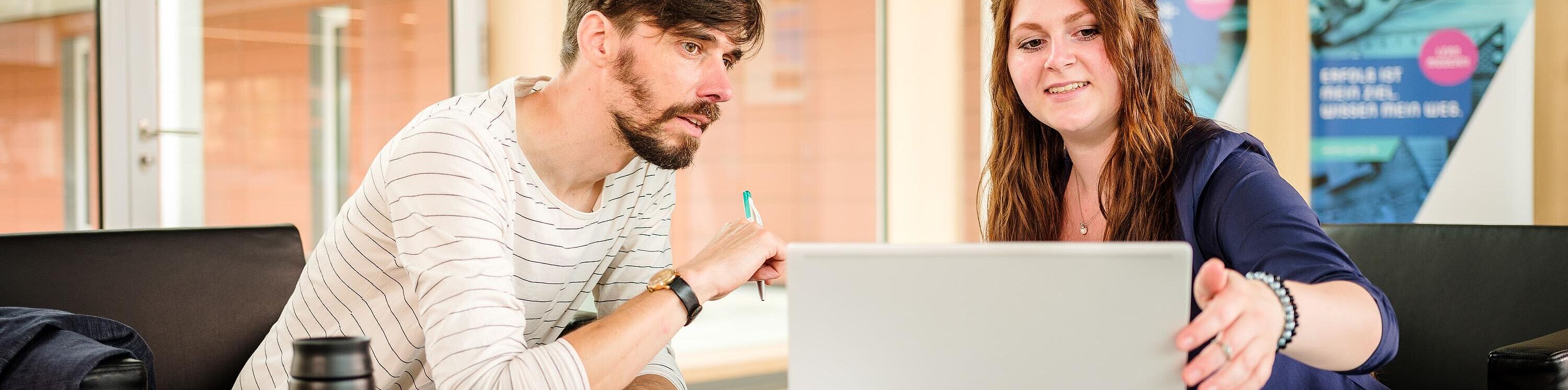 Zwei Personen sitzen beratend an einem Laptop im Foyer des njumii-Gebäudes .