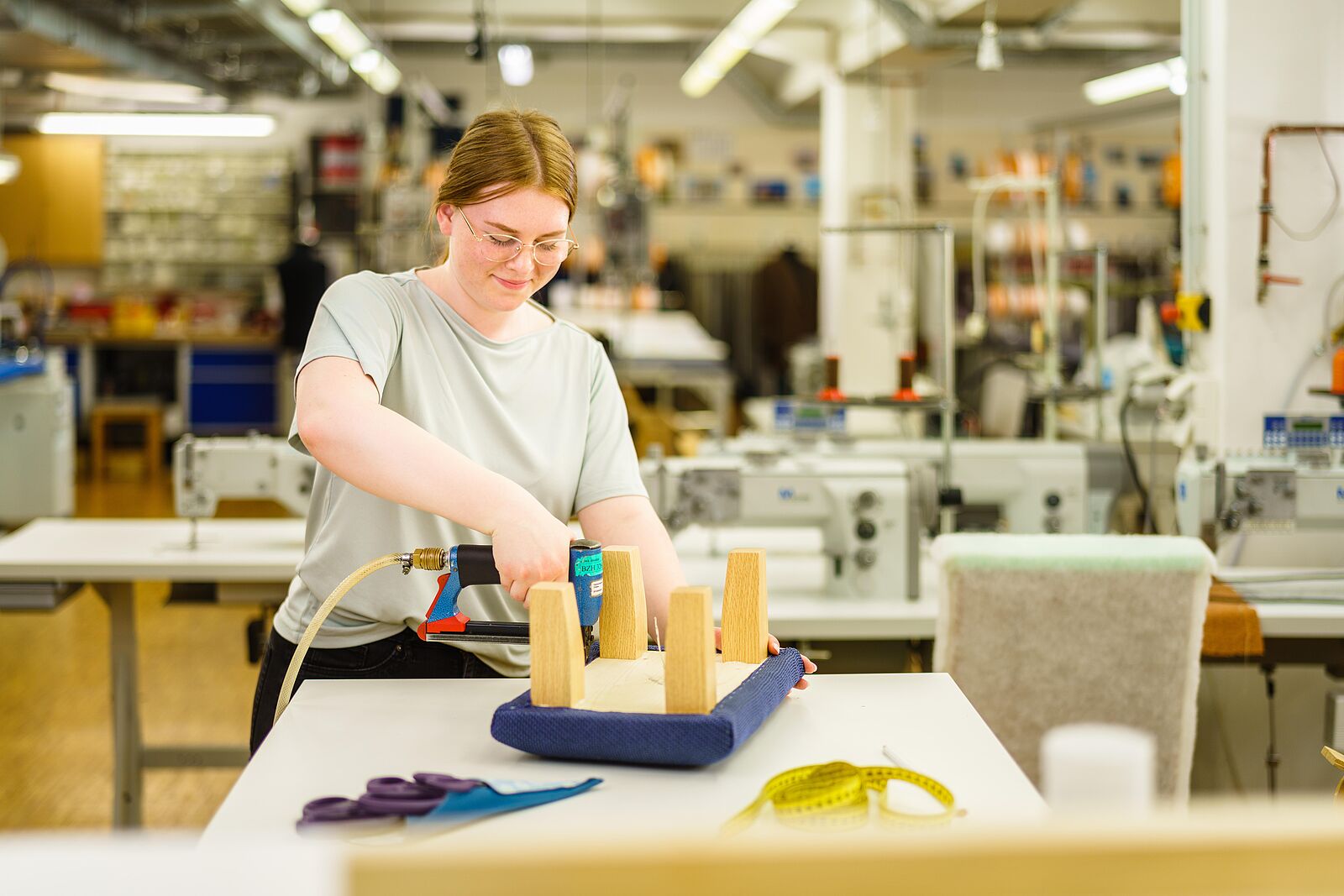 Für  die Herstellung des Junior-Meisterstücks befestigt Alisa N. blauen Stoff an einen Holzhocker mit einem Elektrotacker.