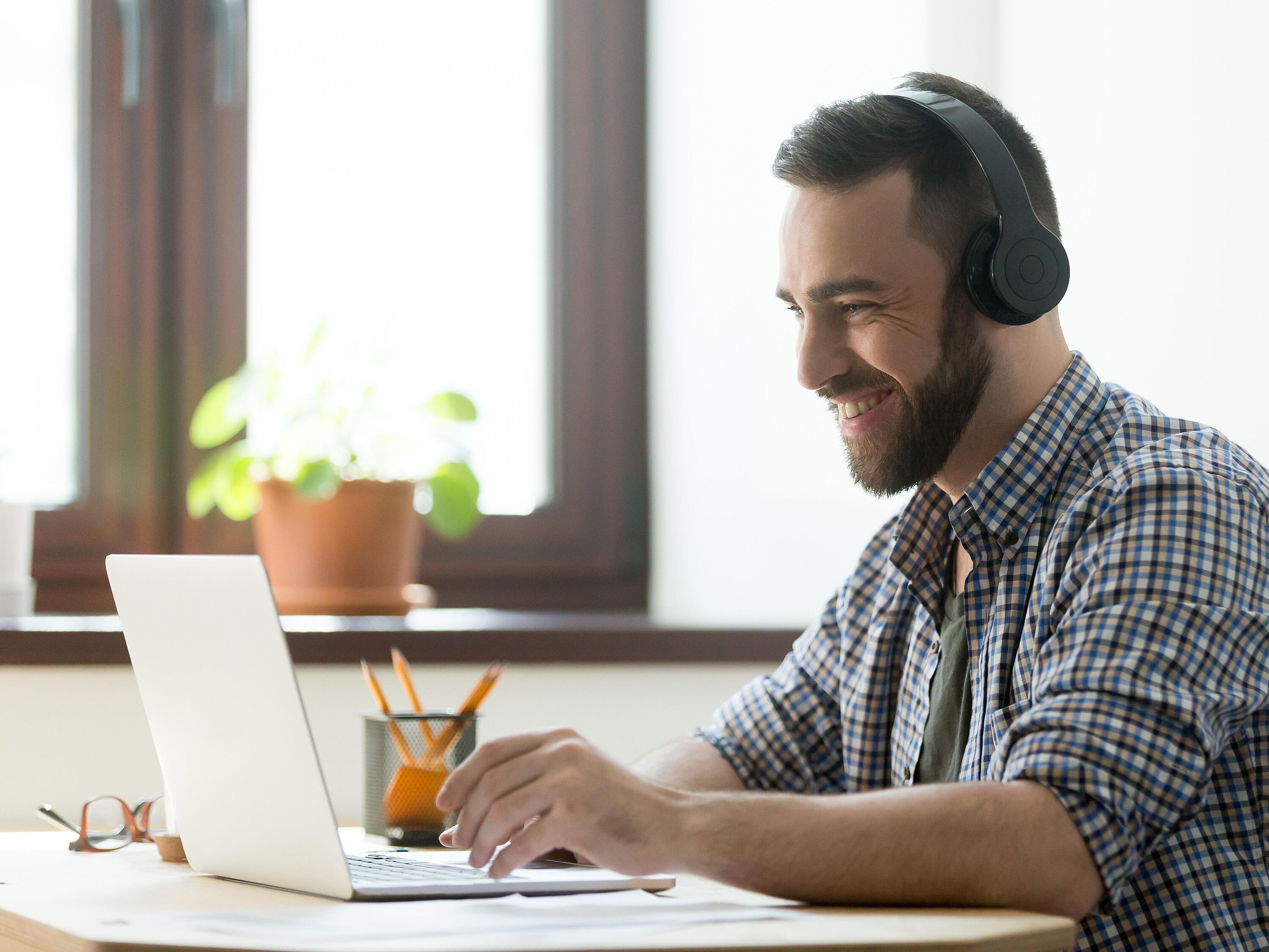 Eine Person sitzt mit Kopfhörern am Schreibtisch vor einem Laptop und verfolgt aktiv ein Webinar.