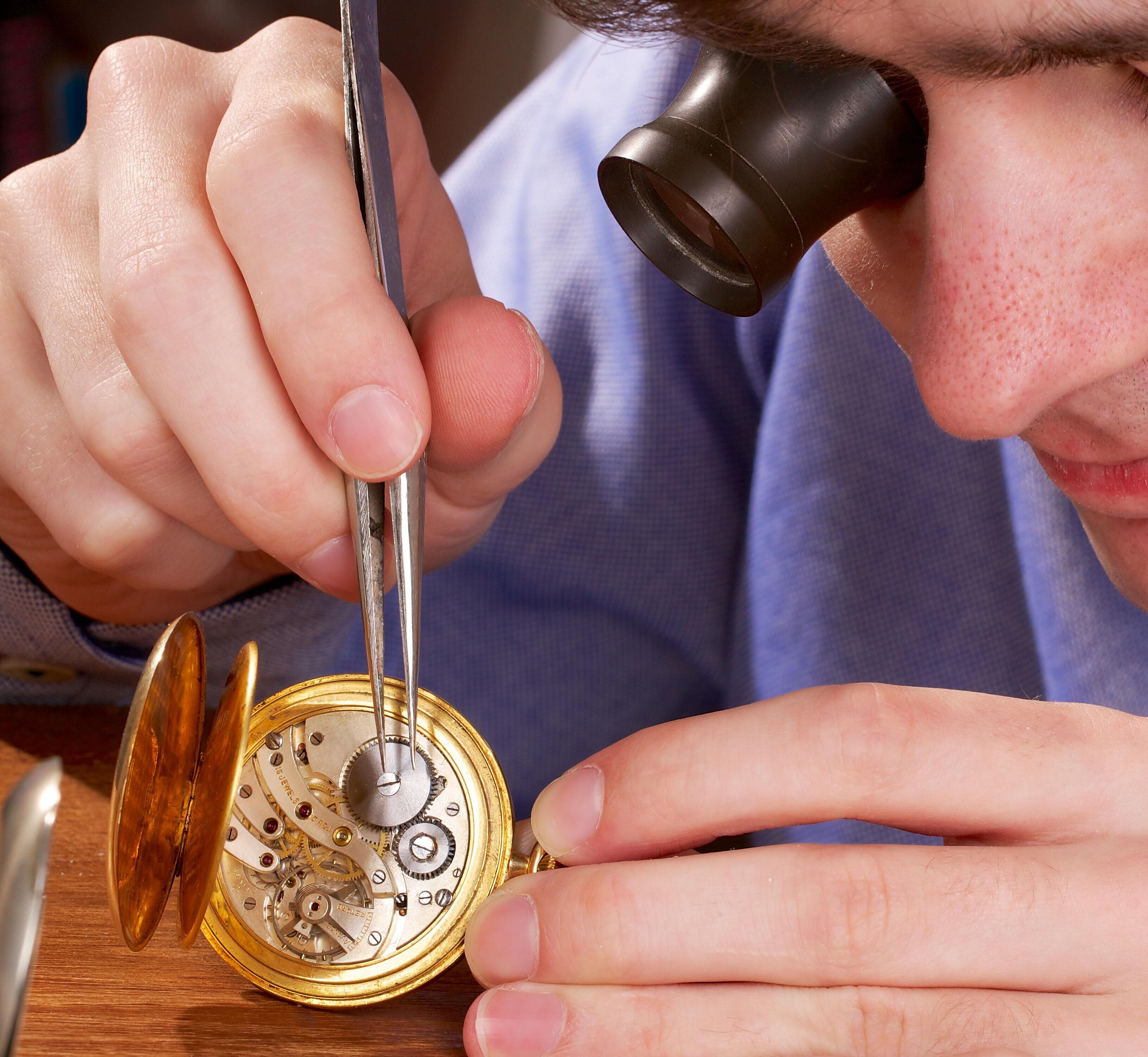 Ein Uhrmacher nimmt an einer geöffneten Uhr Reparaturarbeiten am Uhrwerk vor.